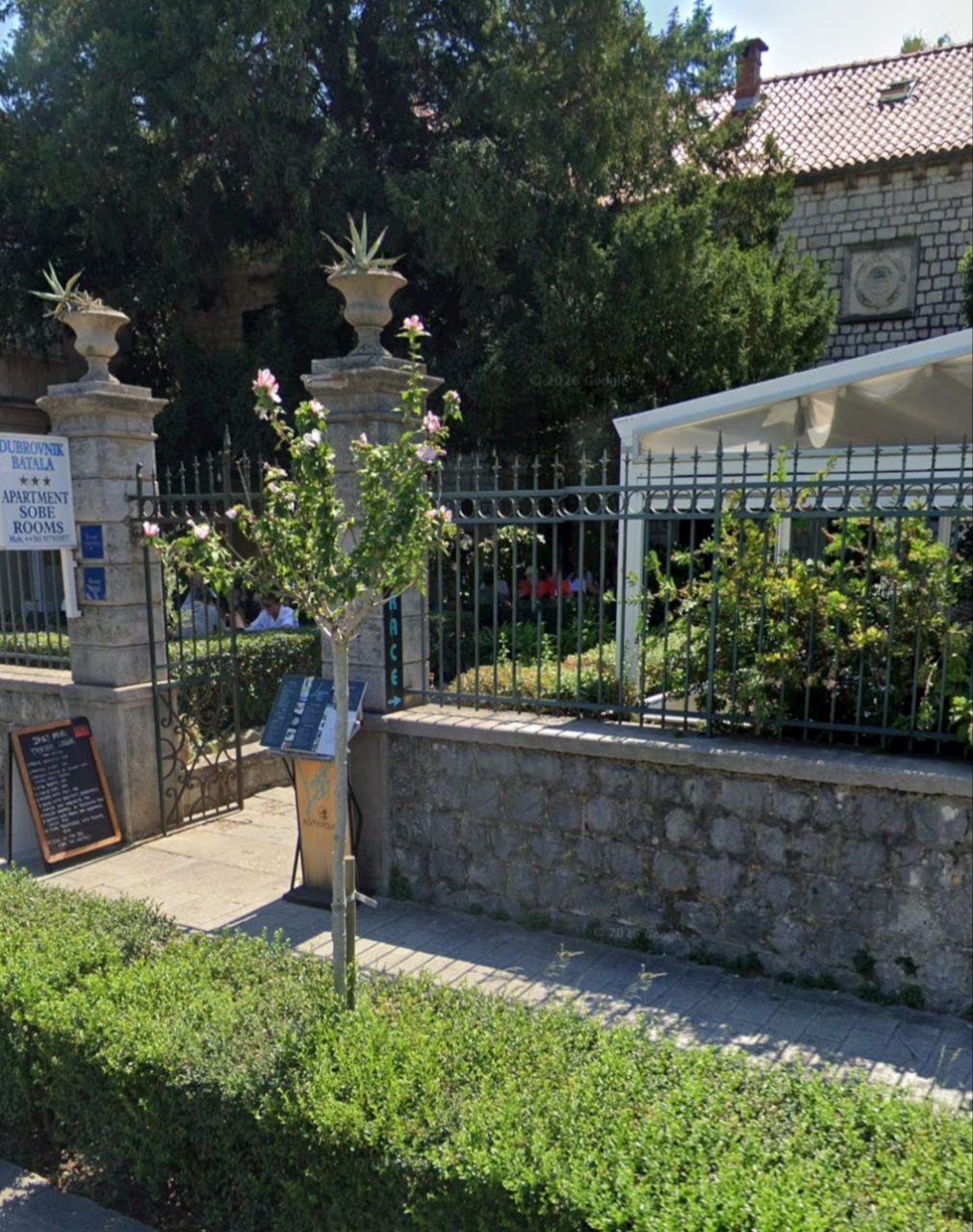 Ulaz u smještaj u Dubrovniku, s kamenim stubovima, metalnom ogradom i natpisom „Apartment Sobe Rooms“.
