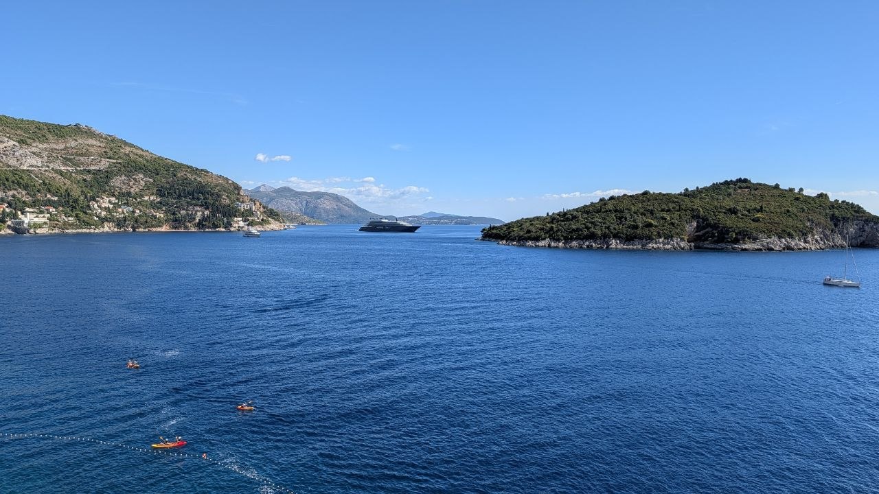 Pogled preko plave uvale na šumovito ostrvo i brodove.