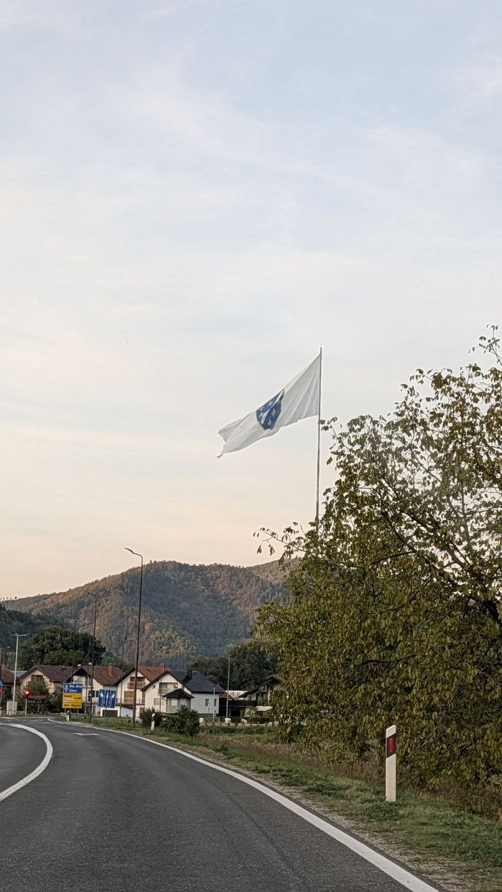 Zavojit seoski put i zastava Bosne i Hercegovine među brdima
