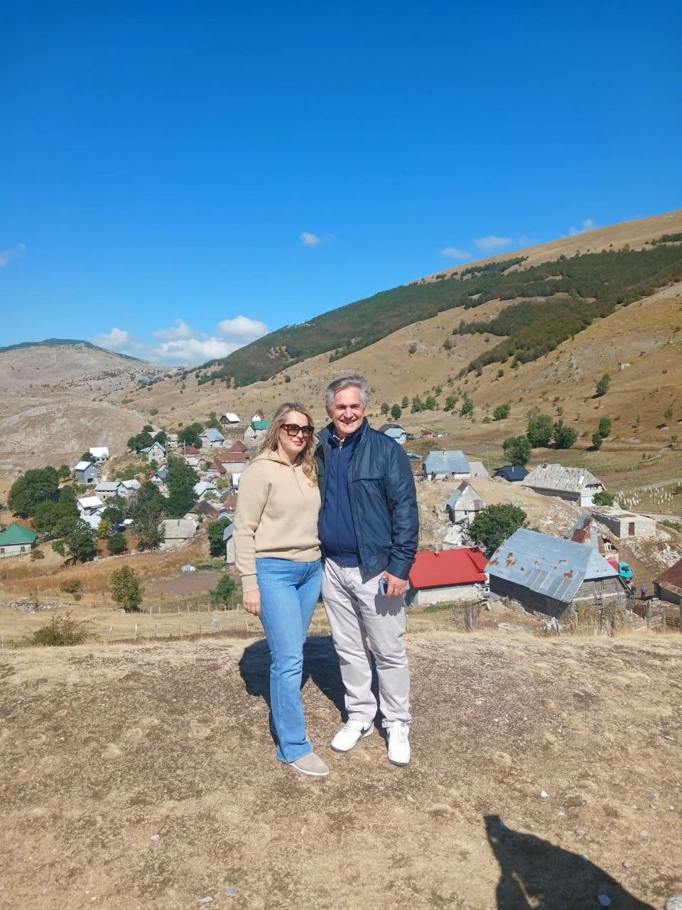 Supružnici stoje iznad planinskog sela s kućama i obroncima u pozadini