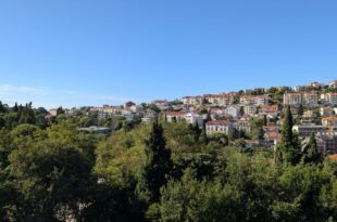 Panorama Dubrovnika s crvenim krovovima i zelenilom u sunčanom danu.
