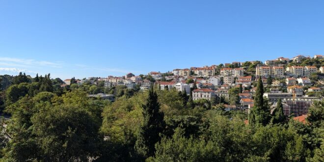 Panorama Dubrovnika s crvenim krovovima i zelenilom u sunčanom danu.