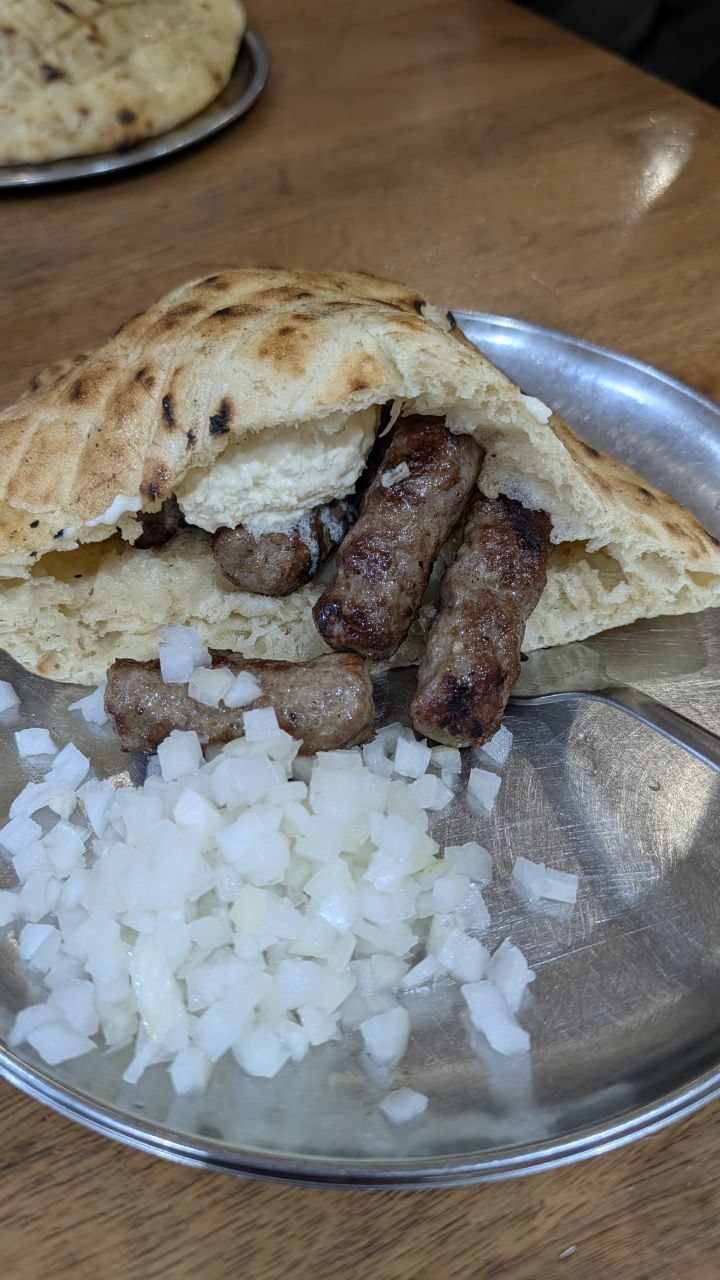 Sarajevski ćevapi u somunu s kajmakom i sjeckanim lukom na metalnom tanjiru