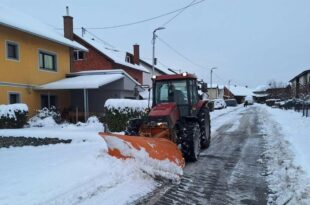 Traktor s ralicom čisti snijeg na ulici tokom zimskih uslova.